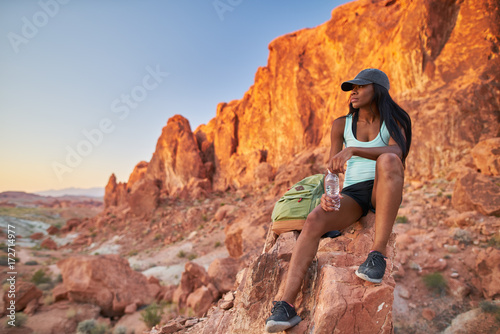 african american woman resting on rock at valley of fire park during hike photo