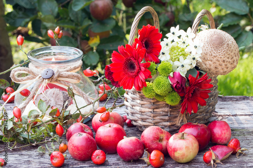 Herbstdekoration mit roten Äpfeln,Herbstblumen im Weidenkorb und Kerze im Glas