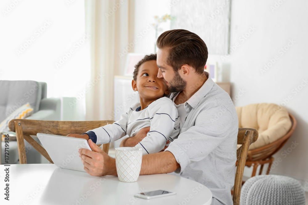 Happy father with adopted African-American boy using tablet computer at home Happy father with adopted African-American boy using tablet computer at home
