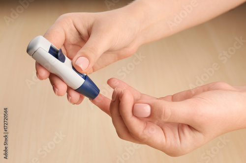 Woman's hands using lancet pen on light background. Diabetes concept
