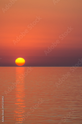 Fototapeta Naklejka Na Ścianę i Meble -  A huge sunset sun in the sky without clouds over the sea.