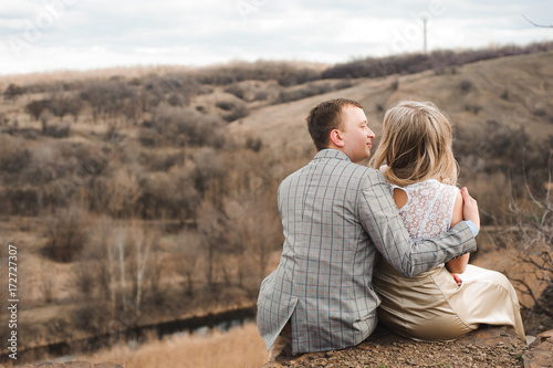 Love, romance and people concept - happy young couple hugging sitting on the edge of a cliff outdoors