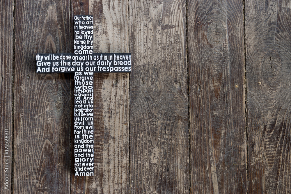 Wooden cross with the Lord's prayer on the shabby  dark brown wooden  plank.