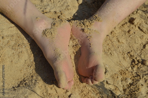 Dirty child's feet in yellow sand photo