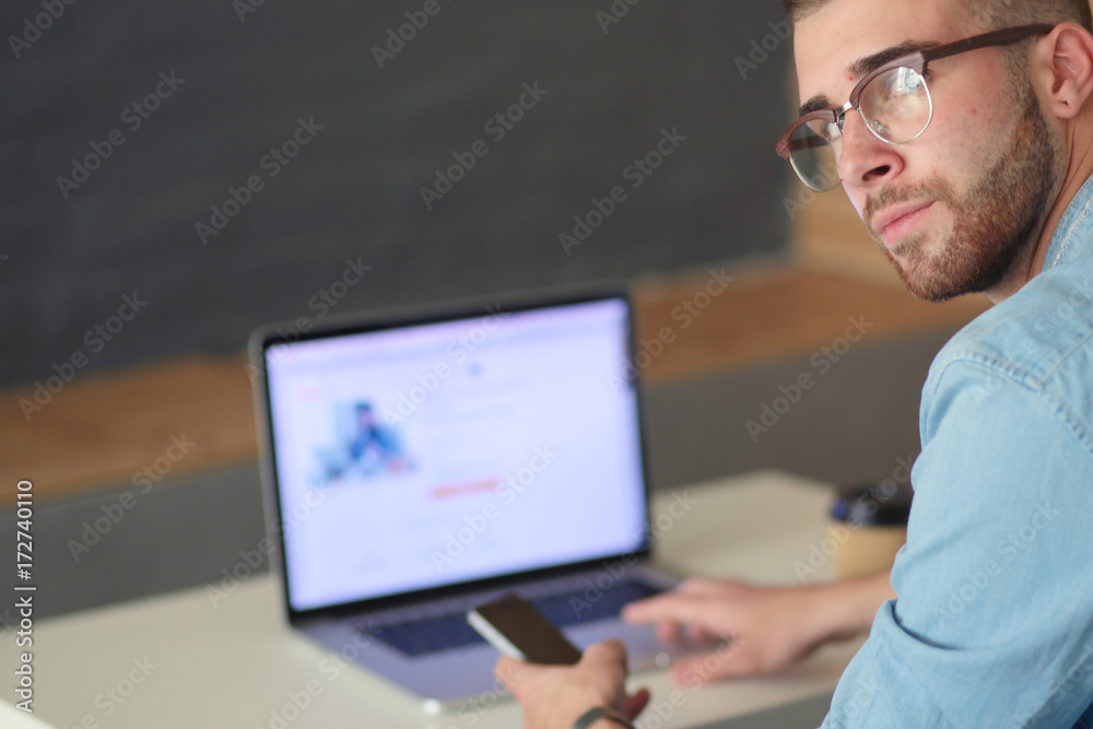 Young man using phone and works on the laptop.