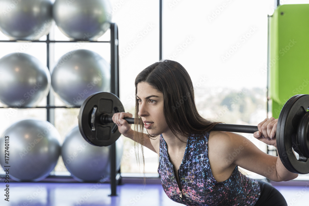 Closeup of female athlete exercising with barbell in a studio Closeup of female athlete exercising with barbell in a studio