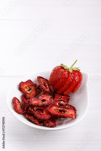 Fresh strawberry and dried strawberry slices on white wooden table.