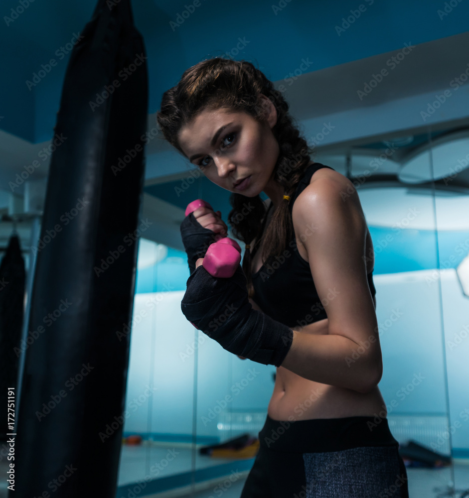 Young fighter boxer girl with hand bandage in training with pink dumbbells. Woman power and beauty