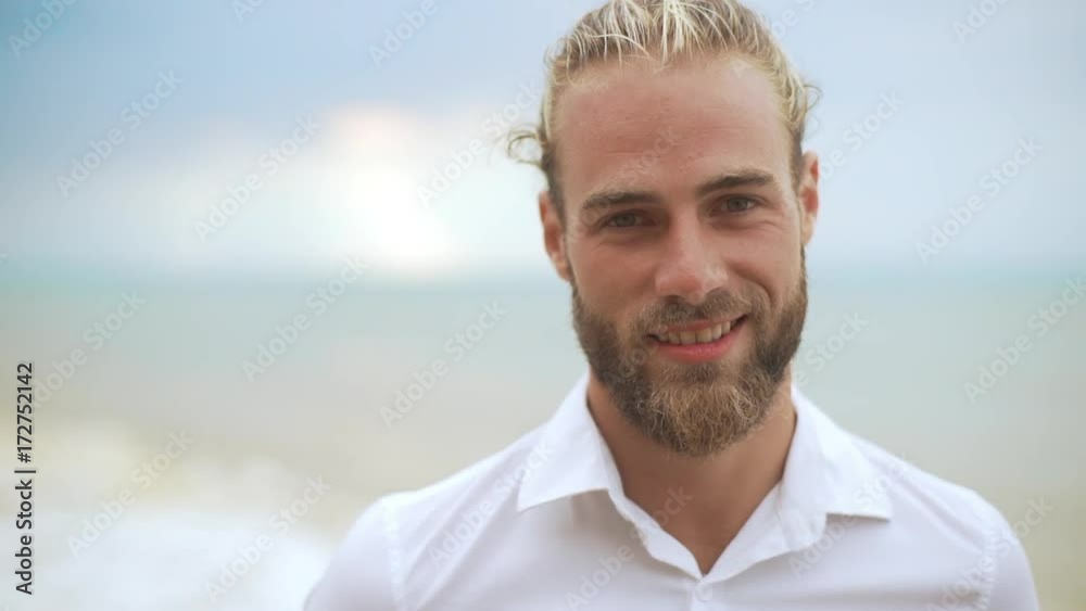 closeup good-looking blond haired gentleman smiling on camera feeling happy with sea on background in defocus in slow motion closeup good-looking blond haired gentleman smiling on camera feeling happy with sea on background in defocus in slow motion