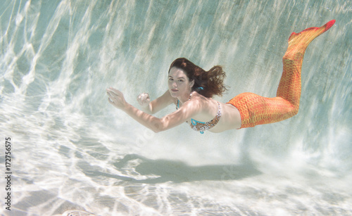 A mermaid with and orange tail underwater.