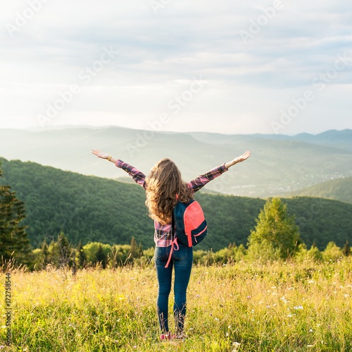 Beautiful young cheerful female model with arms up in mountains