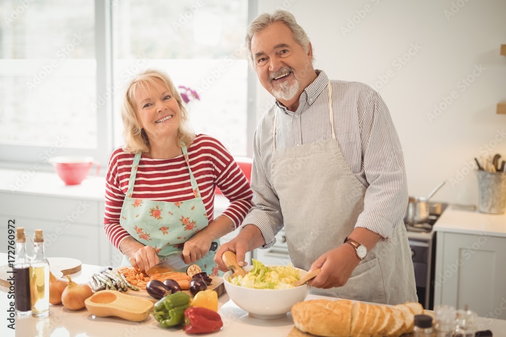 Smiling senior couple preparing salad in kitchen