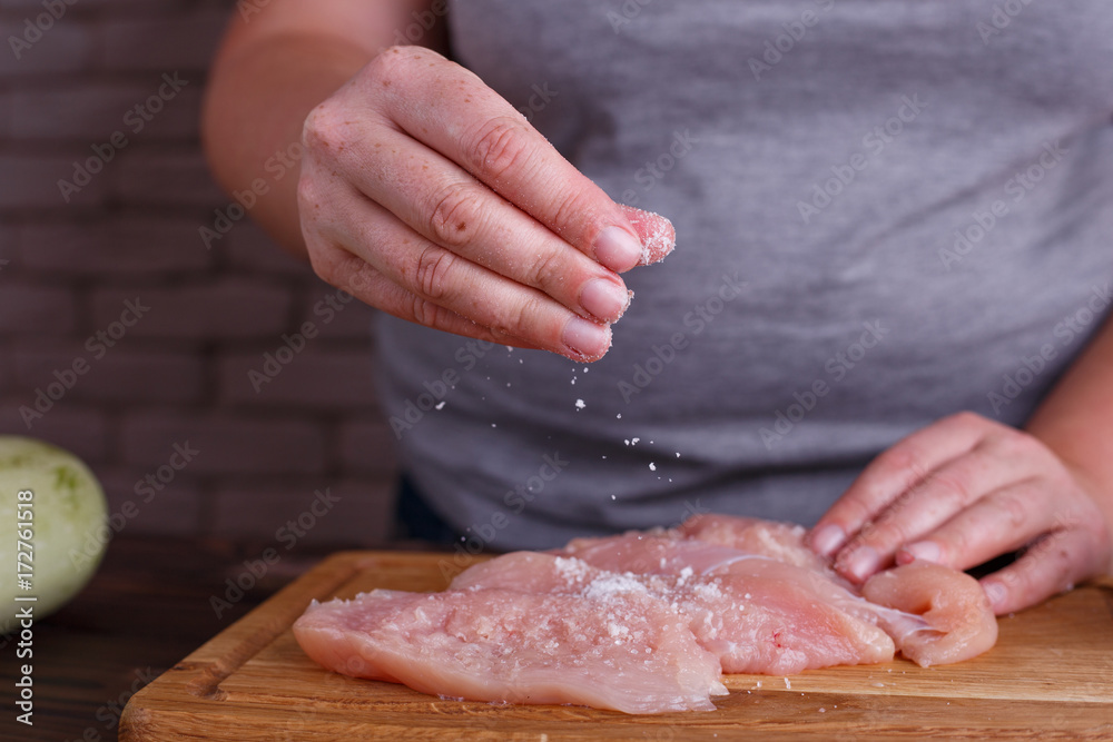 Overweight woman hands adding salt to raw chicken breasts. Dieting, healthy low calorie food, weight losing concept