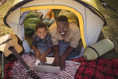 Smiling father and son using laptop in tent