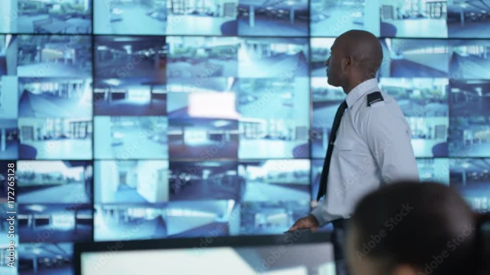  Security team watching CCTV screens in control room, officer talking on radio