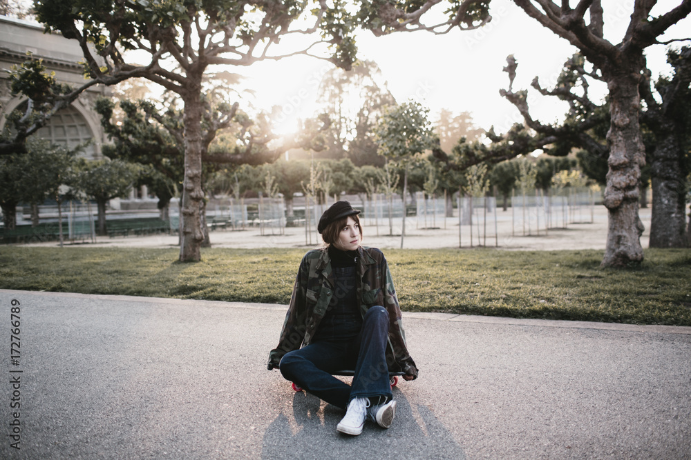 young woman sitting on skateboard in park at sunset young woman sitting on skateboard in park at sunset