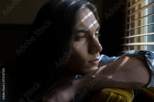 Portrait of young middle eastern man looking out window with bands of light on face photo