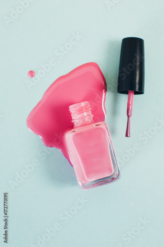 Pink nail polish bottle in puddle of nail polish liquid. photo