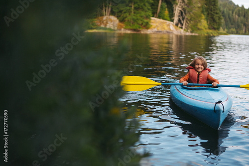 Young caucasian boy enjoying kayak on lake in summer photo