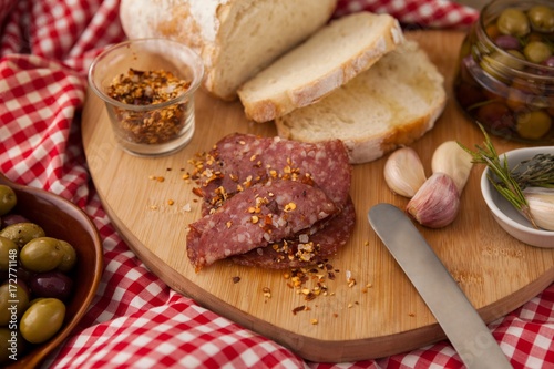 Chili flakes on meat by bread with olives in jar