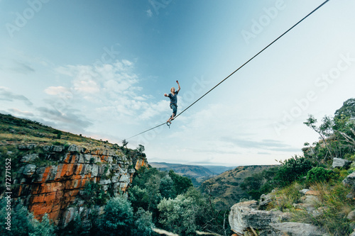 Man tightrope walking a high line over a lush gorge in the mountains photo