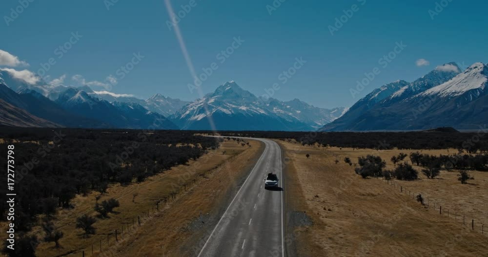 Aerial view of SUV driving in the desert towards snowy mountain peaks in New Zealand
