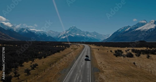 Aerial view of SUV driving in the desert towards snowy mountain peaks in New Zealand
