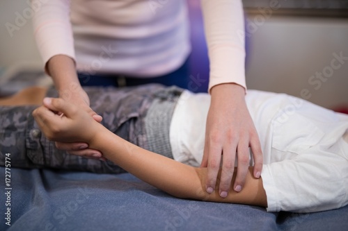 Close-up of female therapist examining hand while boy lying on