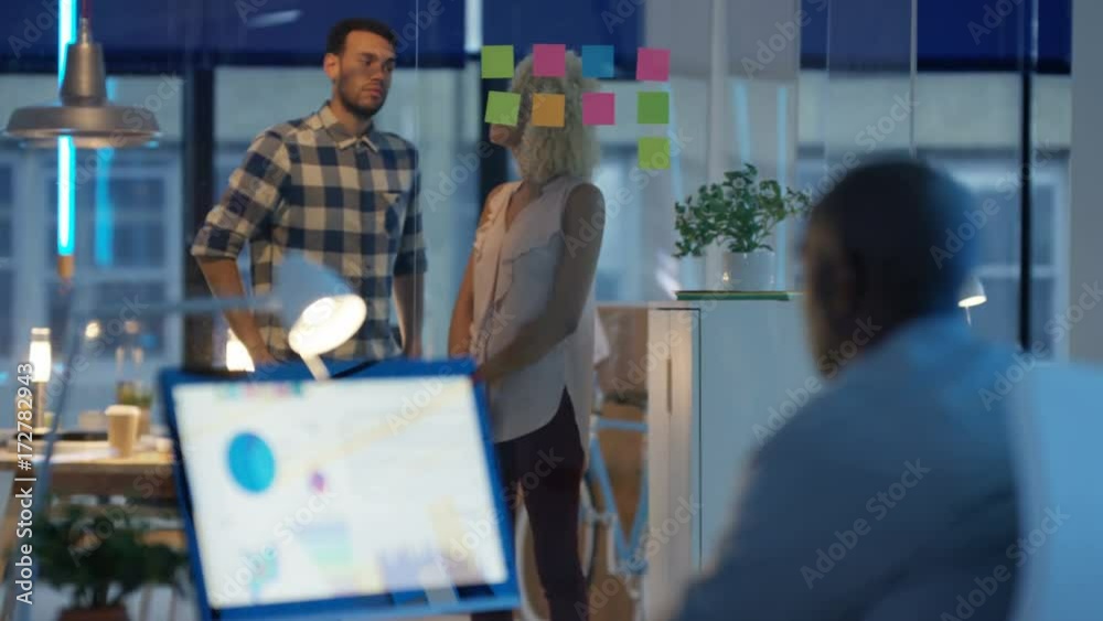 Casual business team in modern office working on computer and brainstorming with sticky notes .