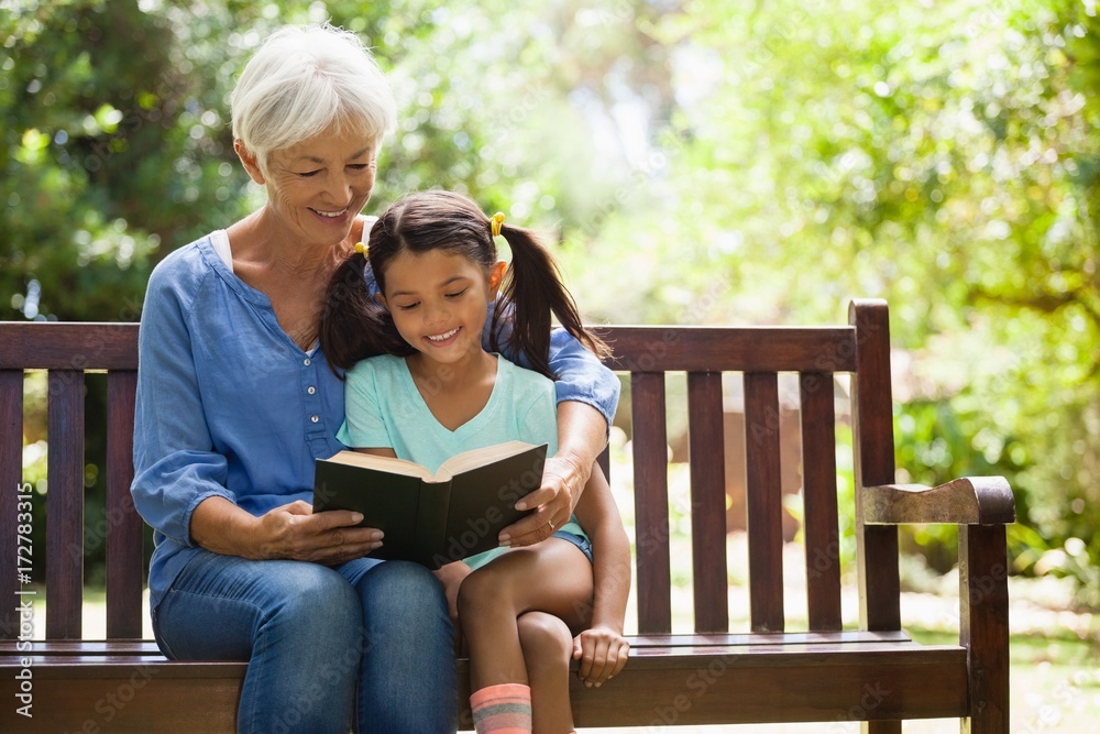Smiling grandmother reading novel to granddaughter sitting on Smiling grandmother reading novel to granddaughter sitting on