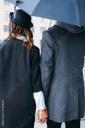 Love couple in rainy day back view. Fashion style. Unrecognizable stylish people in gray and black cloth, moody weather, strong relationship