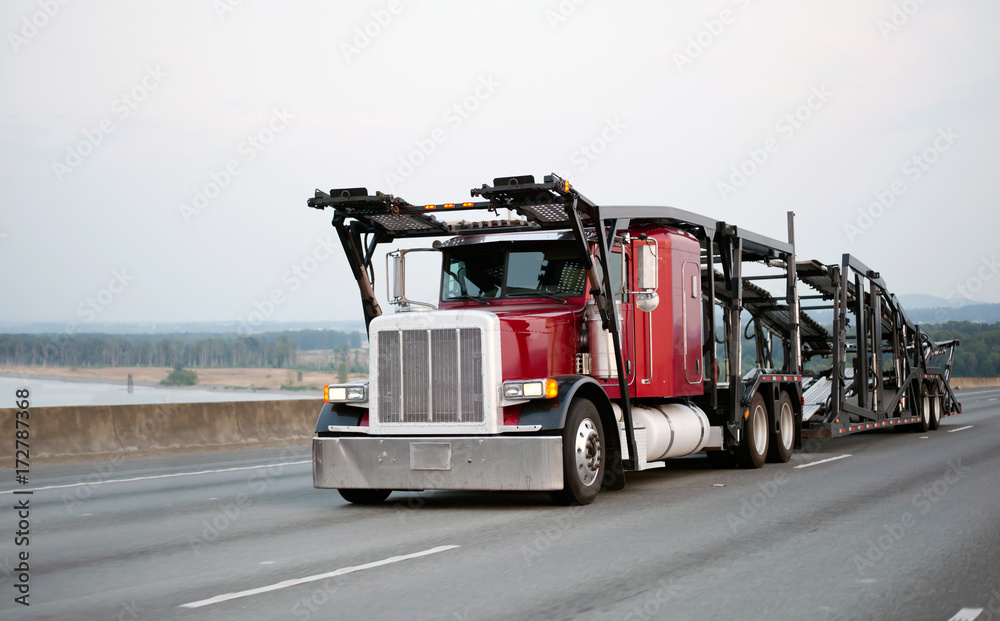 Red classic big rig semi truck with car hauler trailer running by ...