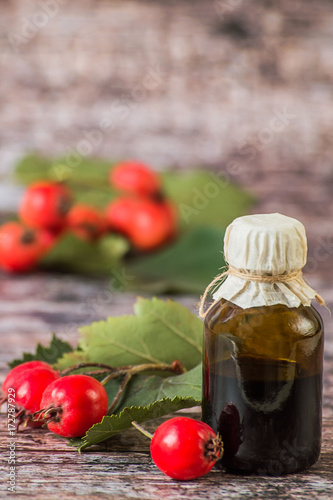     Tincture of hawthorn in a small glass bottle and fresh hawthorn fruit with leaves on a wooden background. Used in folk and traditional medicine.