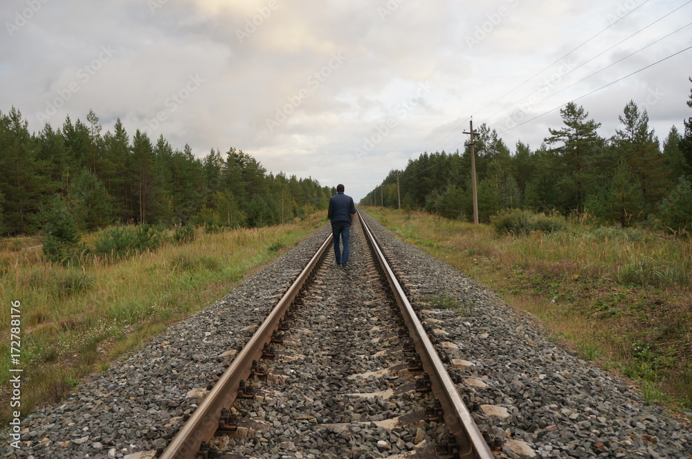 A young man walks along the rails in the forest zone. View from the back