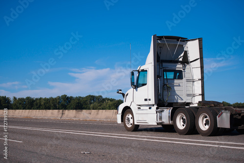 White big rig day cab semi truck with spoilers run on wide interstate highway to warehouse for pick up semi trailer photo