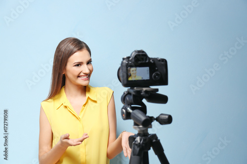 Young female blogger recording video on camera against light background