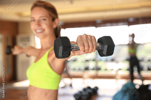 Beautiful young woman training with dumbbells in gym