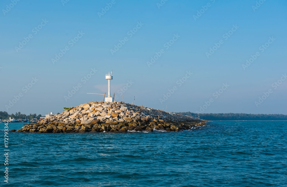 White  lighthouse in the sea in day time and blue sky background . 