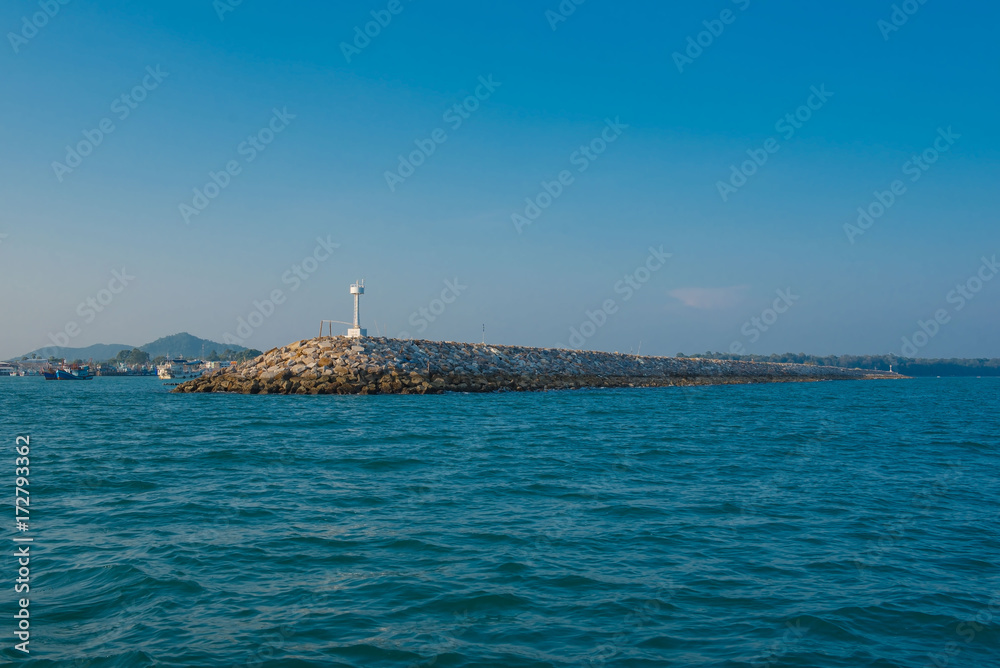 White  lighthouse in the sea in day time and blue sky background . 