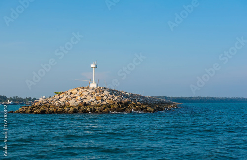 White lighthouse in the sea in day time and blue sky background . 