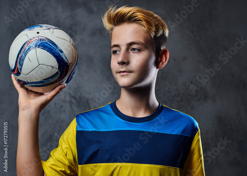 Teenager soccer player dressed in a yellow uniform holds a ball.