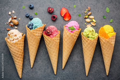 Fototapeta Various of ice cream flavor in cones blueberry ,strawberry ,pistachio ,almond ,orange and cherry setup on dark stone background