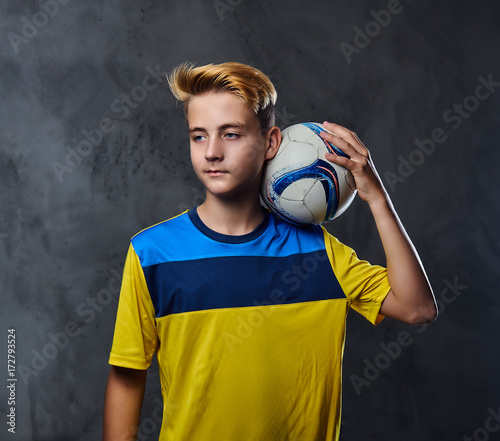 Teenager soccer player dressed in a yellow uniform holds a ball.