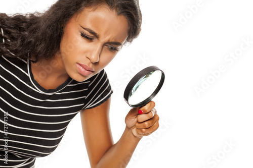 Beautiful young dark skinned woman looking trough the magnifying glass photo
