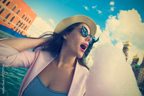 A young woman wearing sunglasses and a hat eating cotton candy outdoor