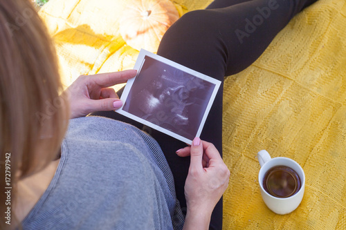 Pregnant woman on the nature, autumn time, sits under a tree in the park, examines the results of an ultrasound examination photo