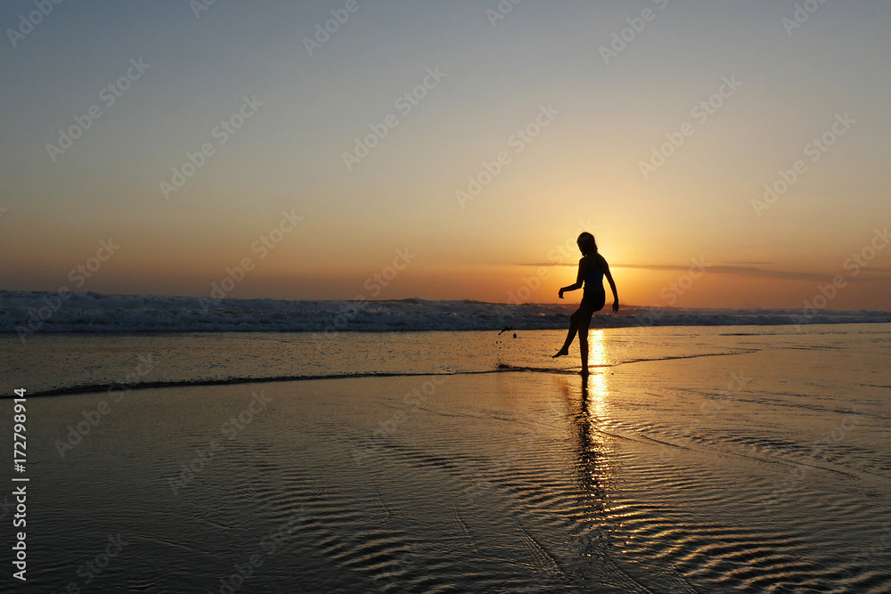 young beautiful Asian girl alone at sea shore looking at orange sky sunset over ocean