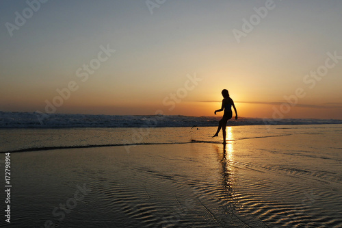 young beautiful Asian girl alone at sea shore looking at orange sky sunset over ocean © Wordley Calvo Stock