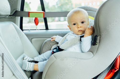 Little cute seriously baby child five month old fastened with security belt in safety car seat
