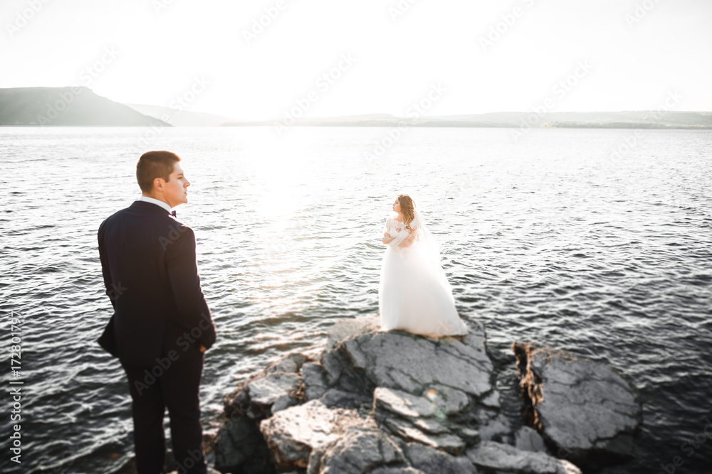 Wedding couple kissing and hugging on rocks near blue sea Wedding couple kissing and hugging on rocks near blue sea